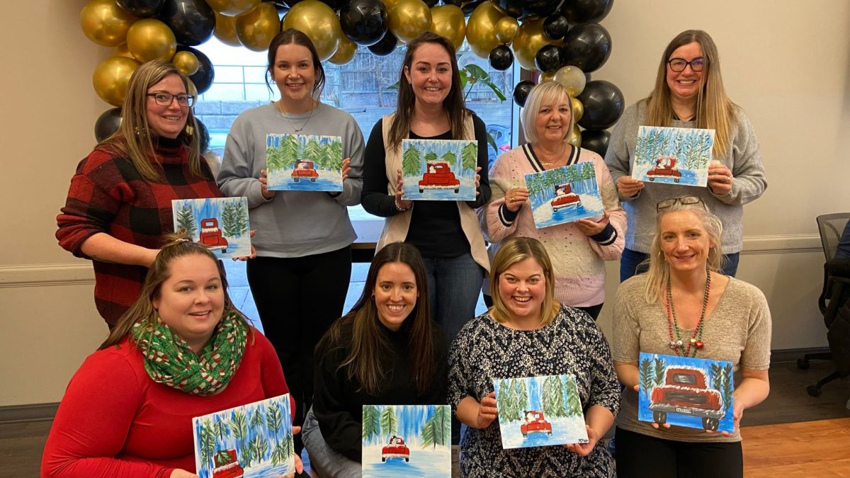 9 people from Early Learning smiling while holding their Christmas paintings.