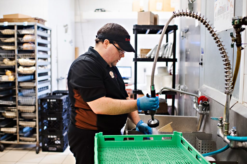 Person supported by KW Career Compass working at Tim Hortons cleaning dishes.