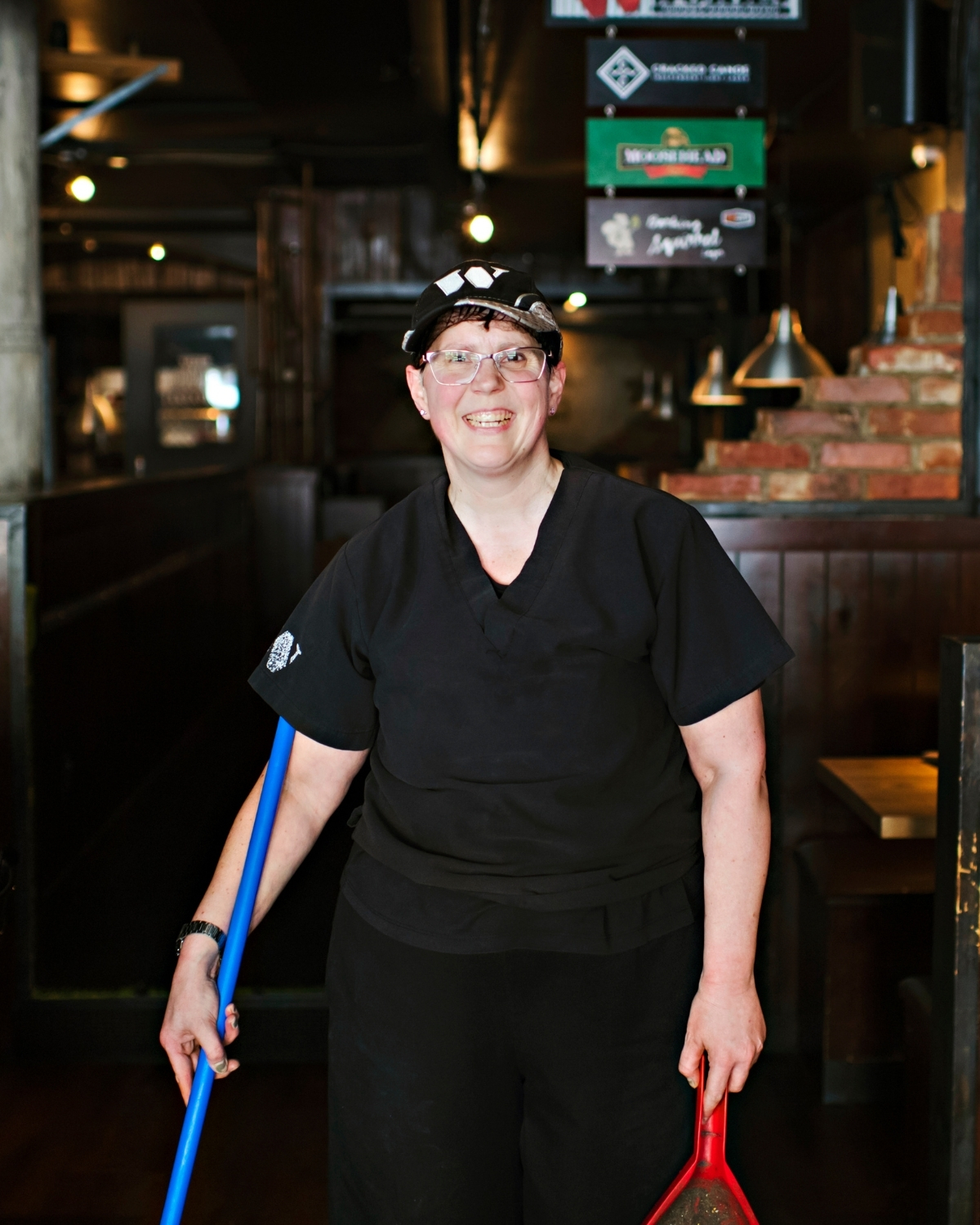 woman in a uniform at a restaurant holding a broom and dust pan
