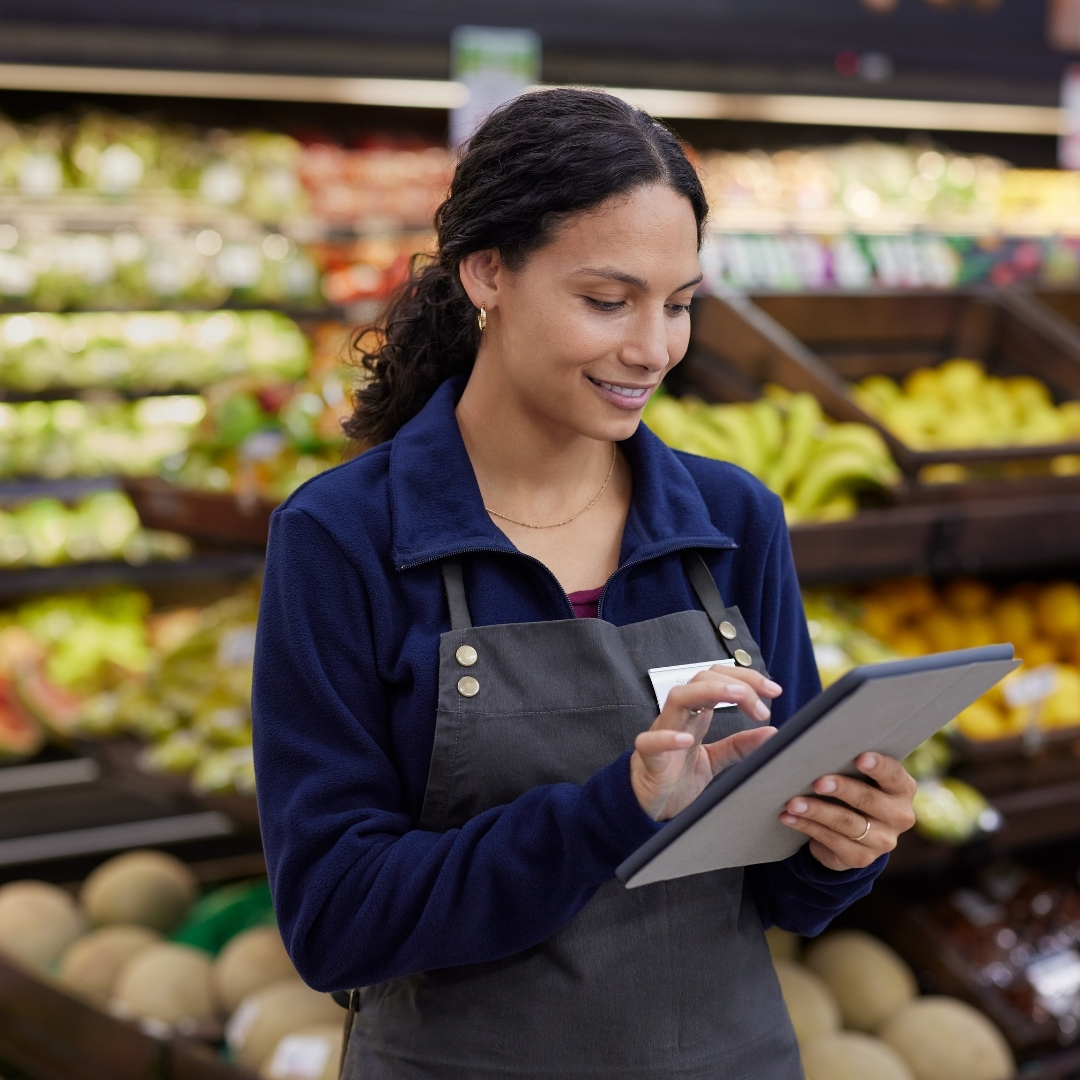 woman working in a grocery store in the produce department holding an iPad