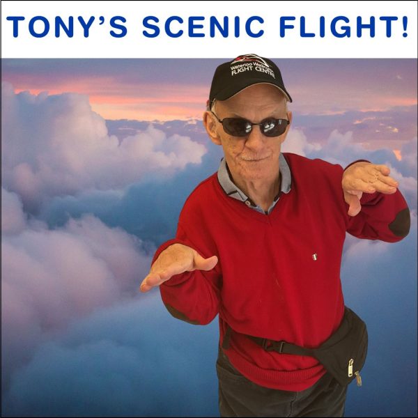Tony posing with his arms out above clouds! Caption says Tony's Scenic Flight