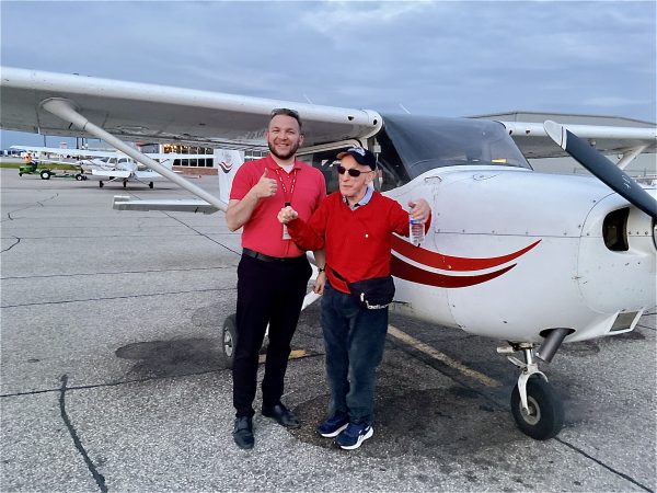 Tony and pilot wearing red shirts and posing beside the white airplane with red stripes!