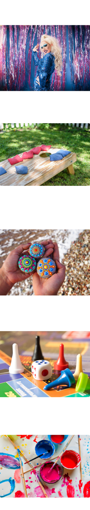 A drag queen. a corn hole board with beanbags on it. A person's hands holding three rocks with mandalas painted on them. Some pieces from a board game. Some paints and paint brushes.