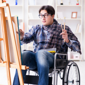 A person using a wheelchair while painting a canvas on an easel