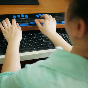 A blind person using a keyboard tailored to make using a computer more accessible.