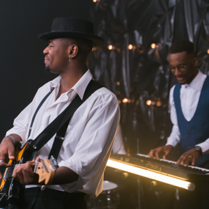 Two musicians. One playing a keyboard and one playing a guitar.