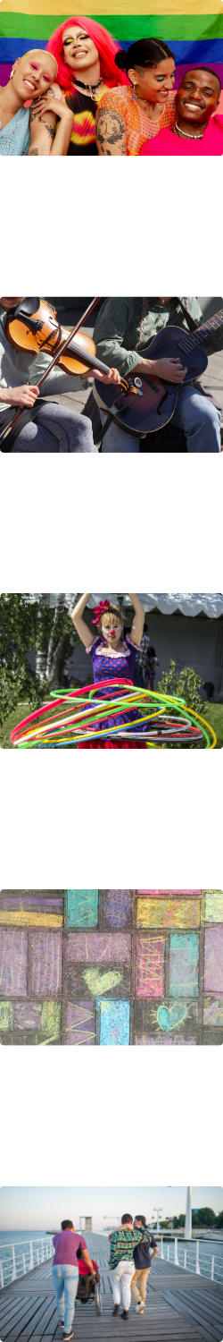 A group of people wearing colourful makeup and clothing smiling together with a rainbow coloured flag in the background. Folk music artists playing both guitar and a fiddle. A performer with many hula hoops at once. A colourful sidewalk chalk art piece. A group of people walking along a boardwalk.