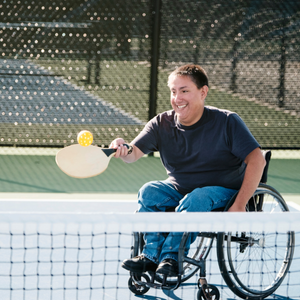 A person using a wheelchair while playing pickleball