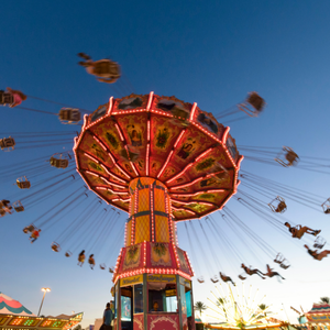 A carnival ride with bright lights swinging people around high above the ground.