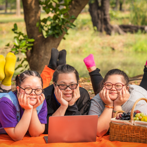 Three people laying on a picnic blanket with a picnic basket next to them.