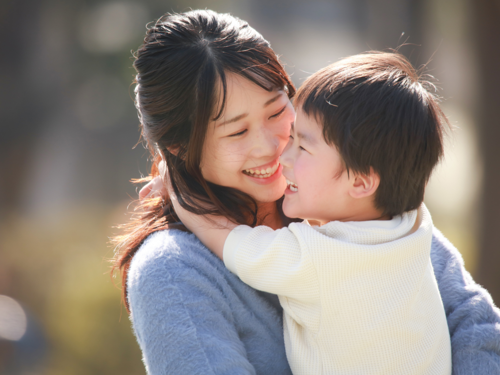 mother and son hugging outside. The son is a toddler and they are smiling at each other