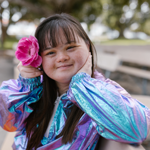 A person smiling and wearing a colourful shirt and flower in their hair.