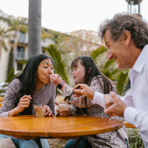 A group of people having fun eating. One person is feeding another person ice cream.