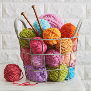 A basket filled with colourful yarn balls and some knitting needles poking out.