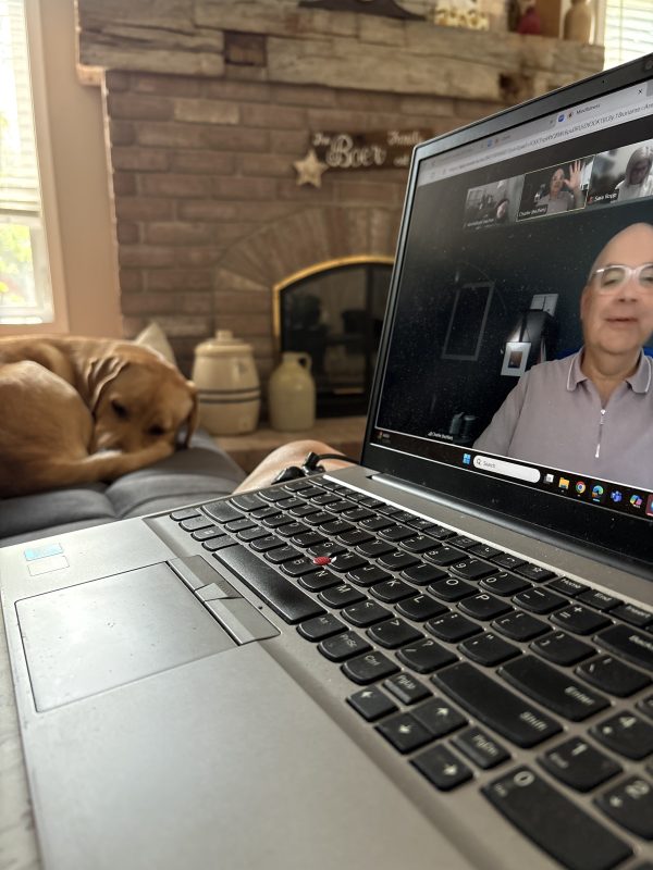 photo of a laptop using zoom. There's a person on the screen. In the background there's a dog sleeping and a fireplace.