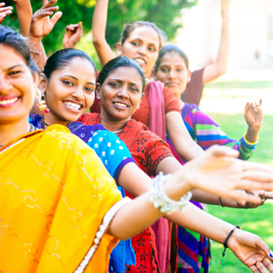 A group of people smiling and holding their arms out. They are dressed in Indian style clothing.