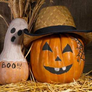 A pumpkin painted with a face and wearing a straw hat. A squash painted lke a ghost with the word "Boo" on it.