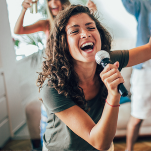 A person smiling and singing into a microphone while dancing with one arm in the air