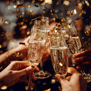 Four glasses of champagne coming together to cheers. Gold confetti is falling all around.