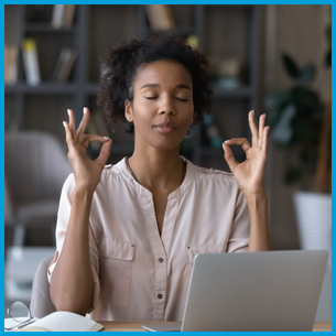 A person with their eyes closed, their elbows on a desk and hands lifted towards their had each with an index finger touching their thumb.