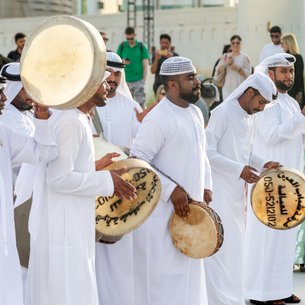 Several people wearing traditional white clothing with hand drums dancing around.