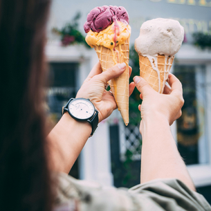 Two ice cream cones being held up, one each in a person's hand.