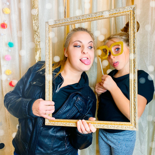 Two people holding a frame and prop glasses to make a funny photo at a photo booth.