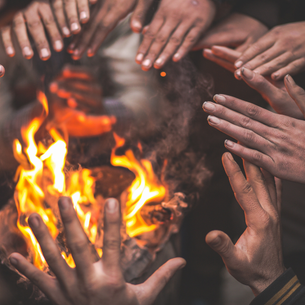 A fire with people's hands all around it getting warmed up.