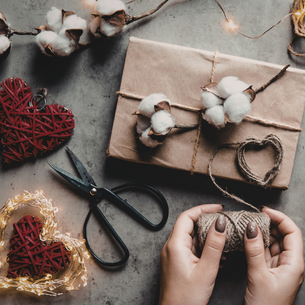 A person's hands and some craft supplies including scissors, cotton balls and some hearts that look like they are woven out of branches and painted red.