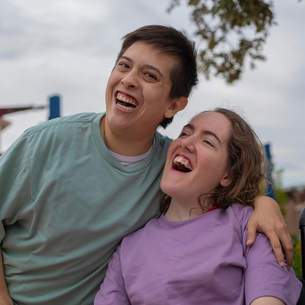 Two people smiling. One has their arm around the other.
