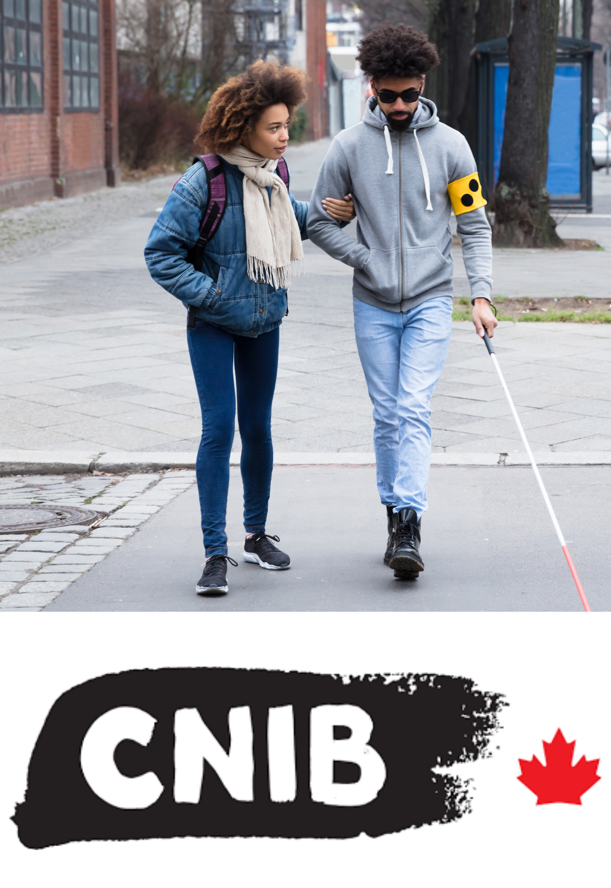 A person with dark glasses on using a white cane. Another person is gently guiding them as they walk across a crosswalk with their hand on the person's elbow.