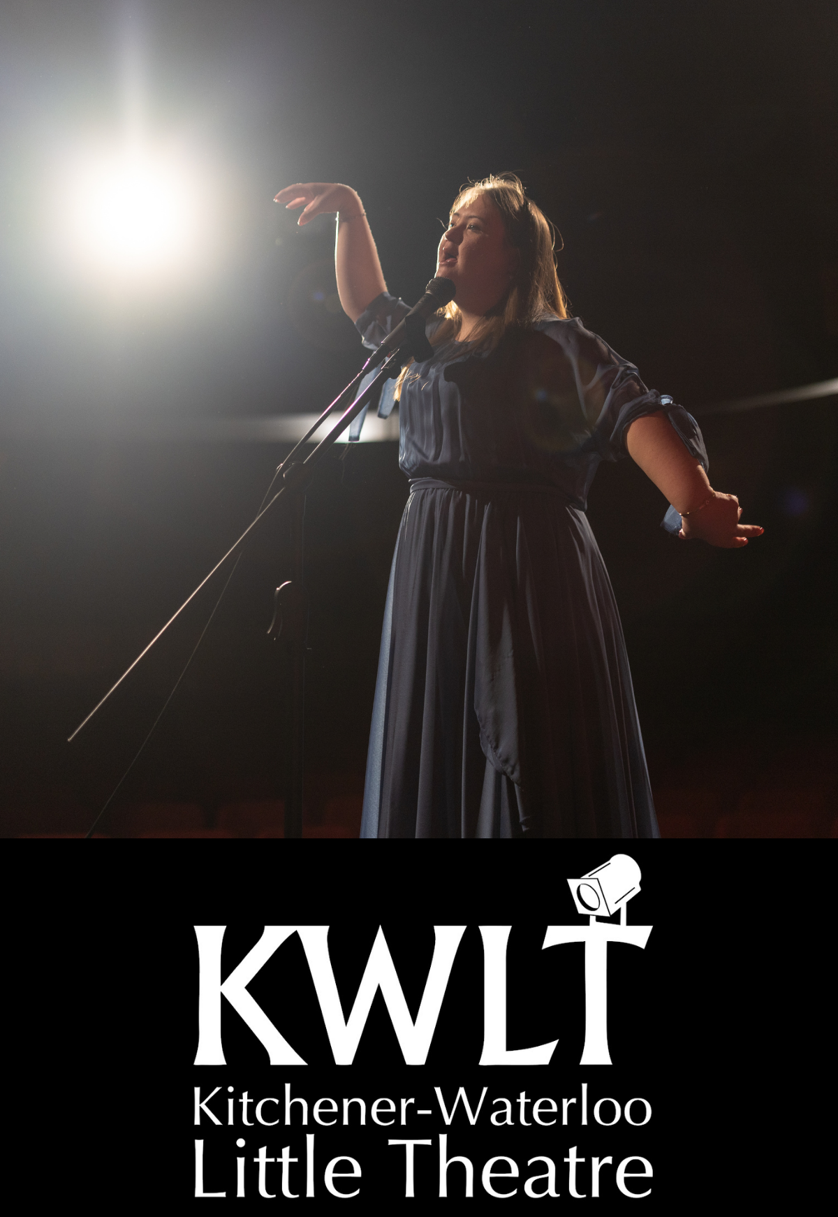 a person on stage performing with a microphone on a stand. there is a spot light shining on the person.