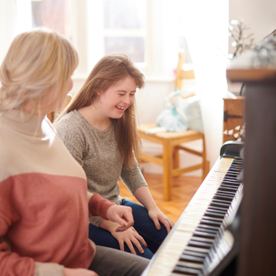 Two people sitting in front of a piano. One is smiling. The other has their head turned to look at the person smiling.
