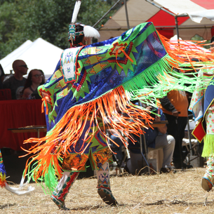 A person wearing a large colourful piece of cloth with many ribbons across the bottom dangling and blowing in the wind as they dance.