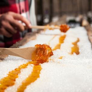 Maple taffy being made from maple syrup being poured on ice and rolled up with a wooden spoon.
