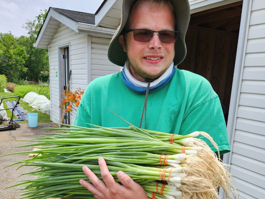 a smiling man holding a harvest of green onions