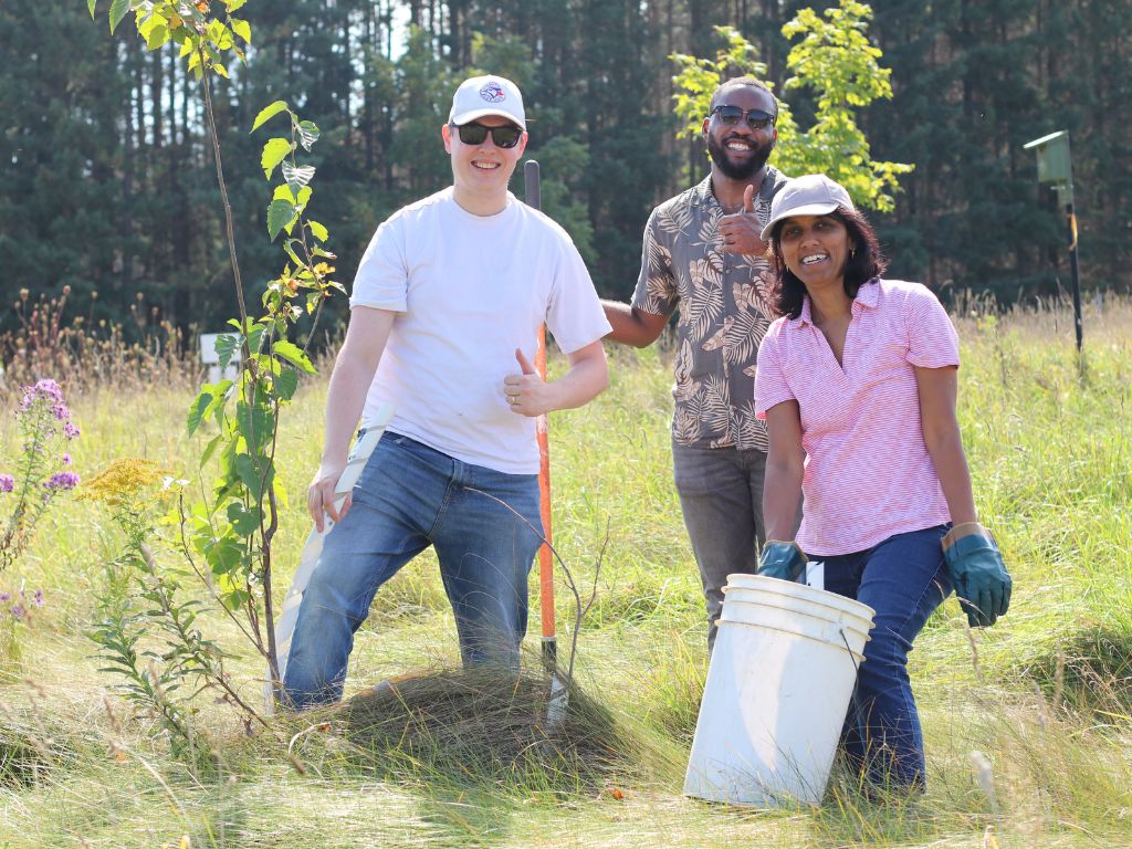 three people standing and smiling in a farmers field