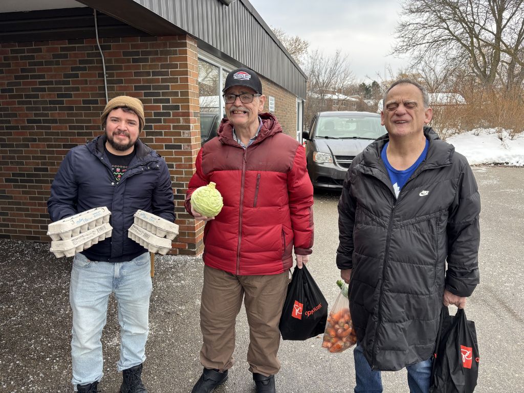 three people standing in a parking lot holding eggs and vegetables