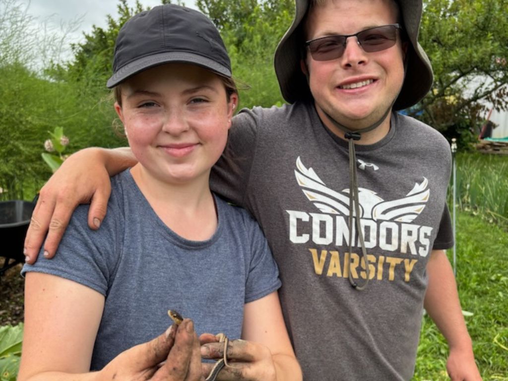 two young people smiling in a farmers field holding a small snake