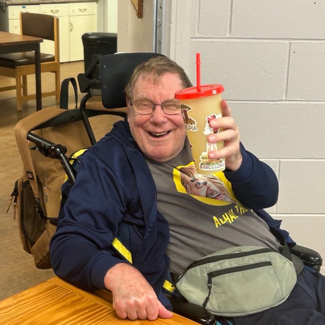 smiling man in wheelchair holding a reusable cup with a straw