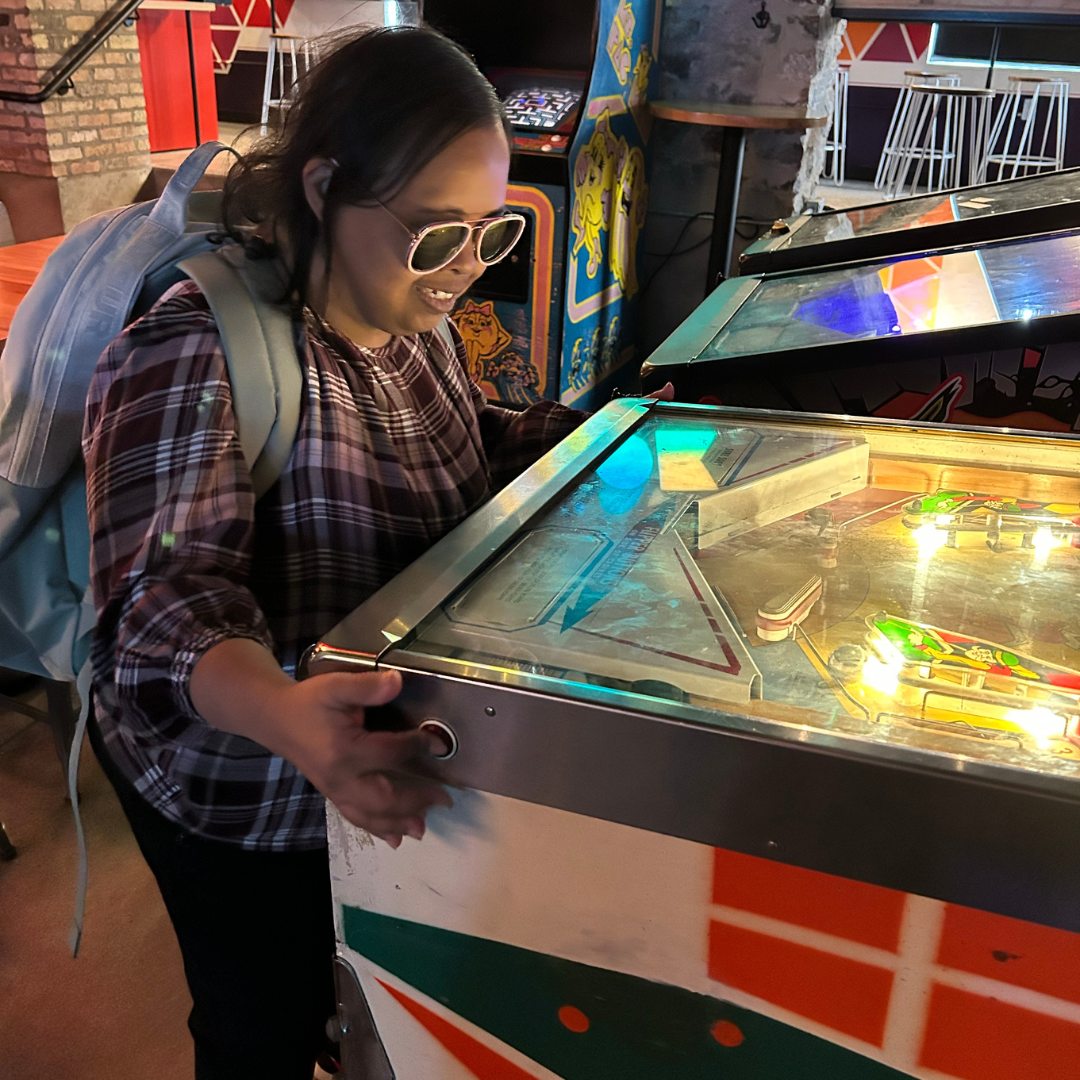 photo of a woman with sunglasses on playing pinball. she is an icon.
