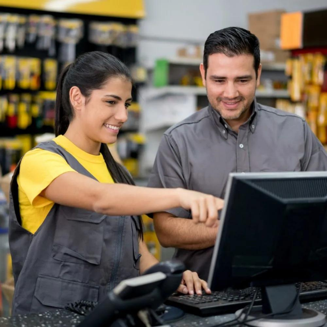 photo of two people in a store at a cash register. One woman and one man. The woman is showing the man something on the cash register/montior