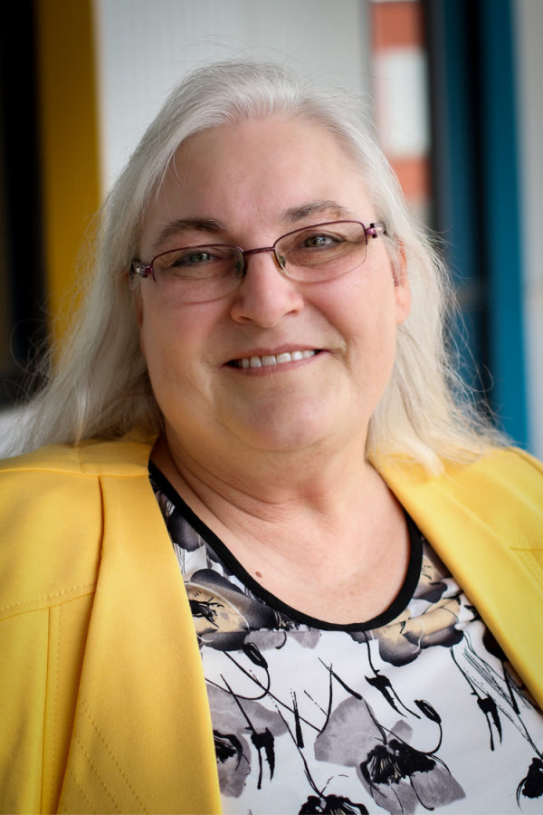 Headshot of Ana Golobic, a white woman with grey hair smiling and friendly. She is wearing a yellow blazer.