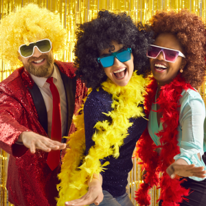 Hangout Events SHOP PHOTOS-2 photo of three people in front of a yellow backdrop. they're wearing fun wigs and feather boas and sunglasses